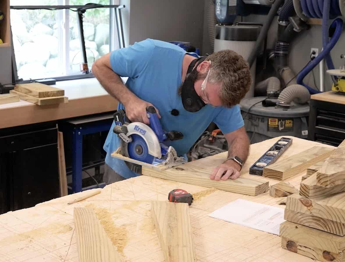 Cutting a 2x4 back support blank with a circular saw, finished parts stacked on the bench