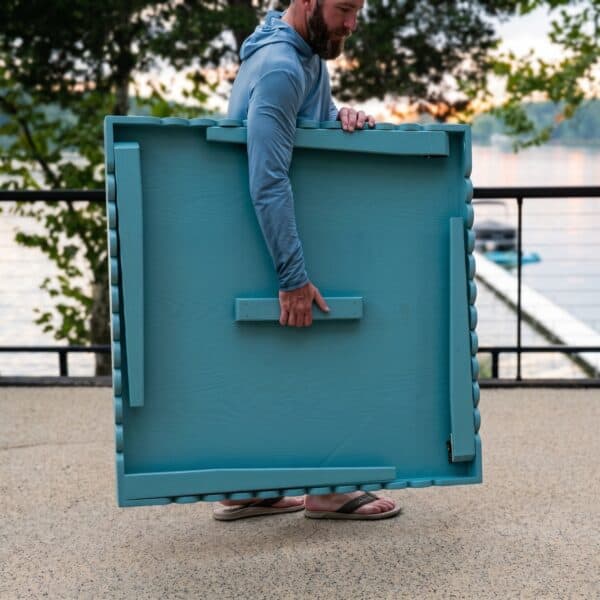 Carrying the folded mahjong table in one hand, legs folded flat underneath