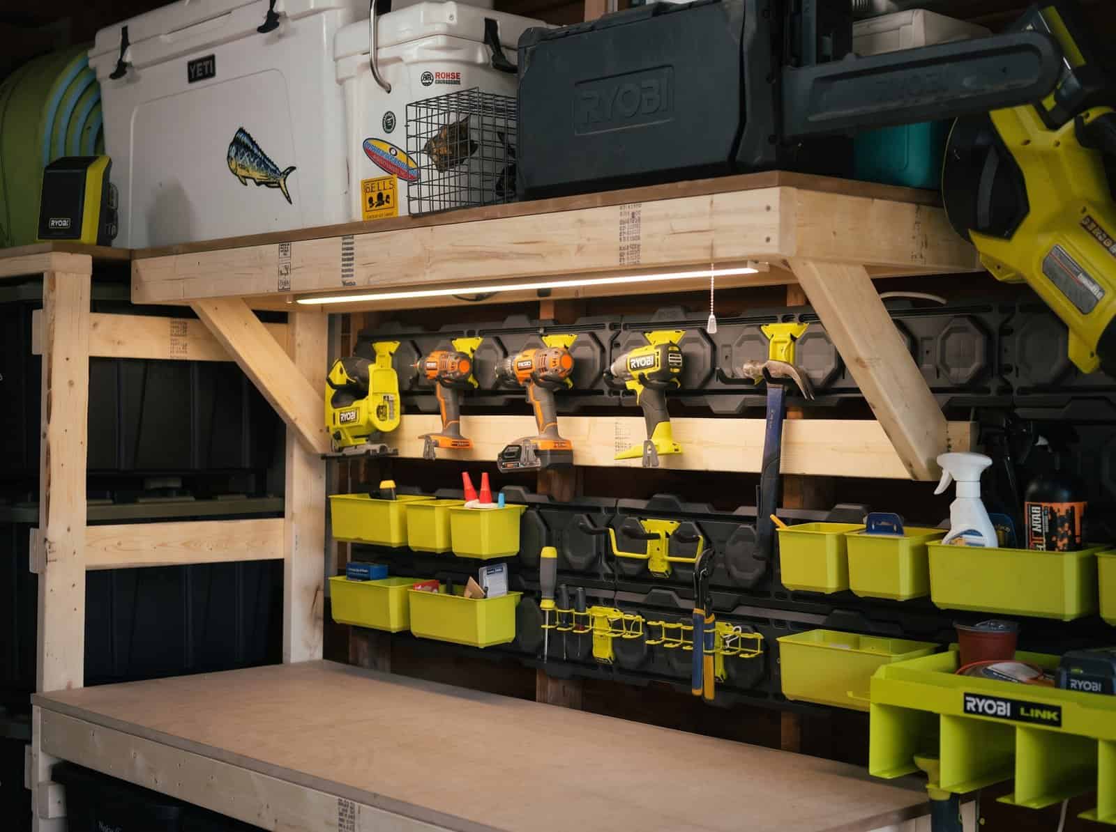 DIY garage shelf built from 2x4s and plywood above a workbench, holding coolers and tool cases