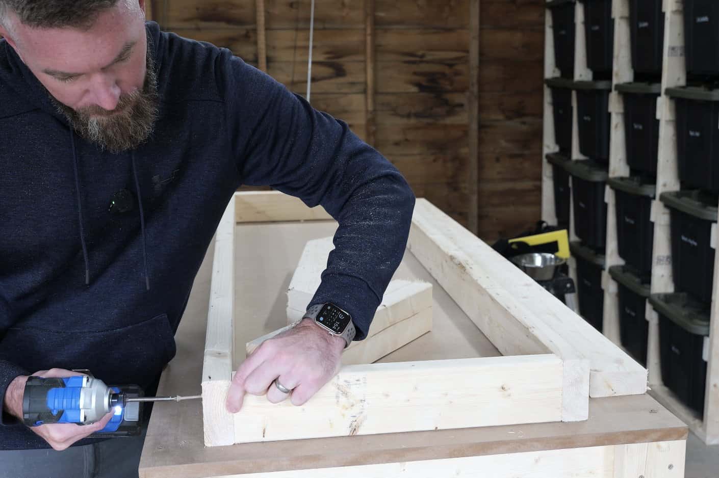 Screwing 2x4 cross pieces between the ledger and front rail to build the workbench shelf frame