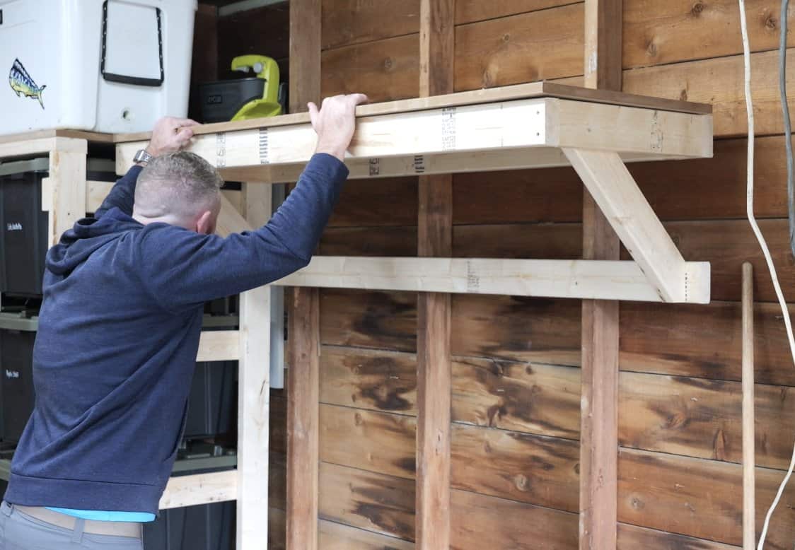 Setting the plywood top onto the finished 2x4 garage shelf above the workbench