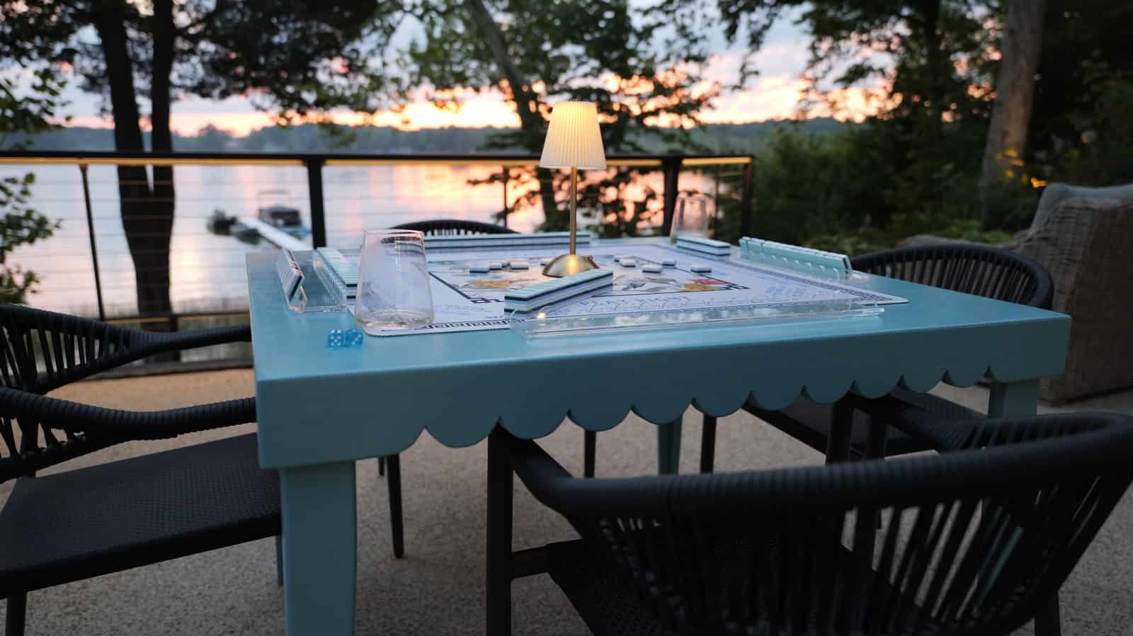 DIY mahjong table painted blue with a scalloped apron and tapered legs, set with a mahjong mat and tiles on a patio at sunset